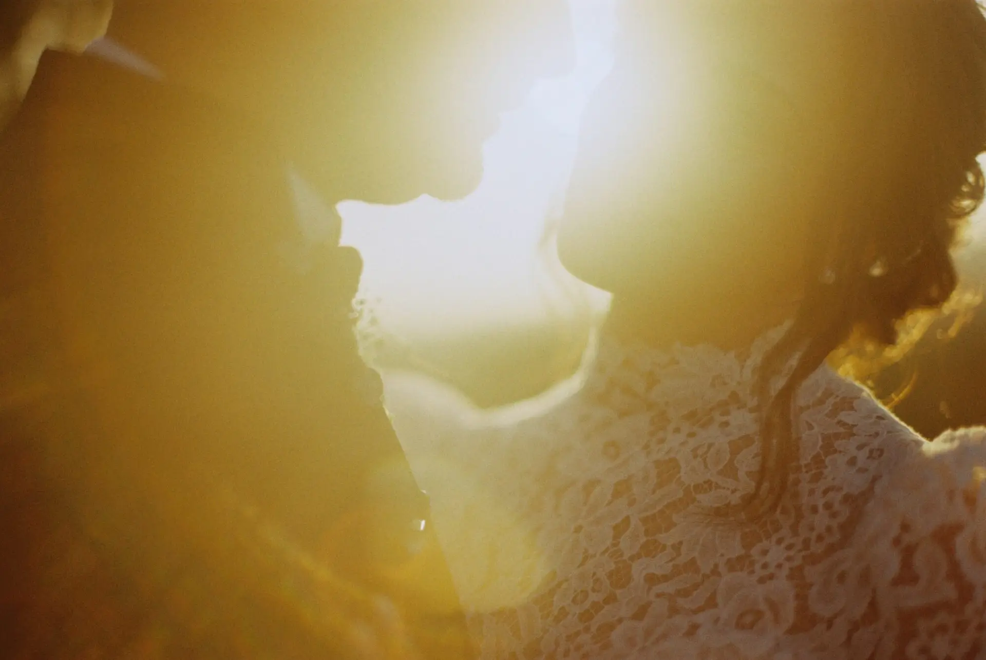 Ritratto intimo degli sposi in forte controluce (flare) al tramonto. Fotografia di matrimonio scattata a pellicola con estetica sognante. Fotografo Daniele Pullara.