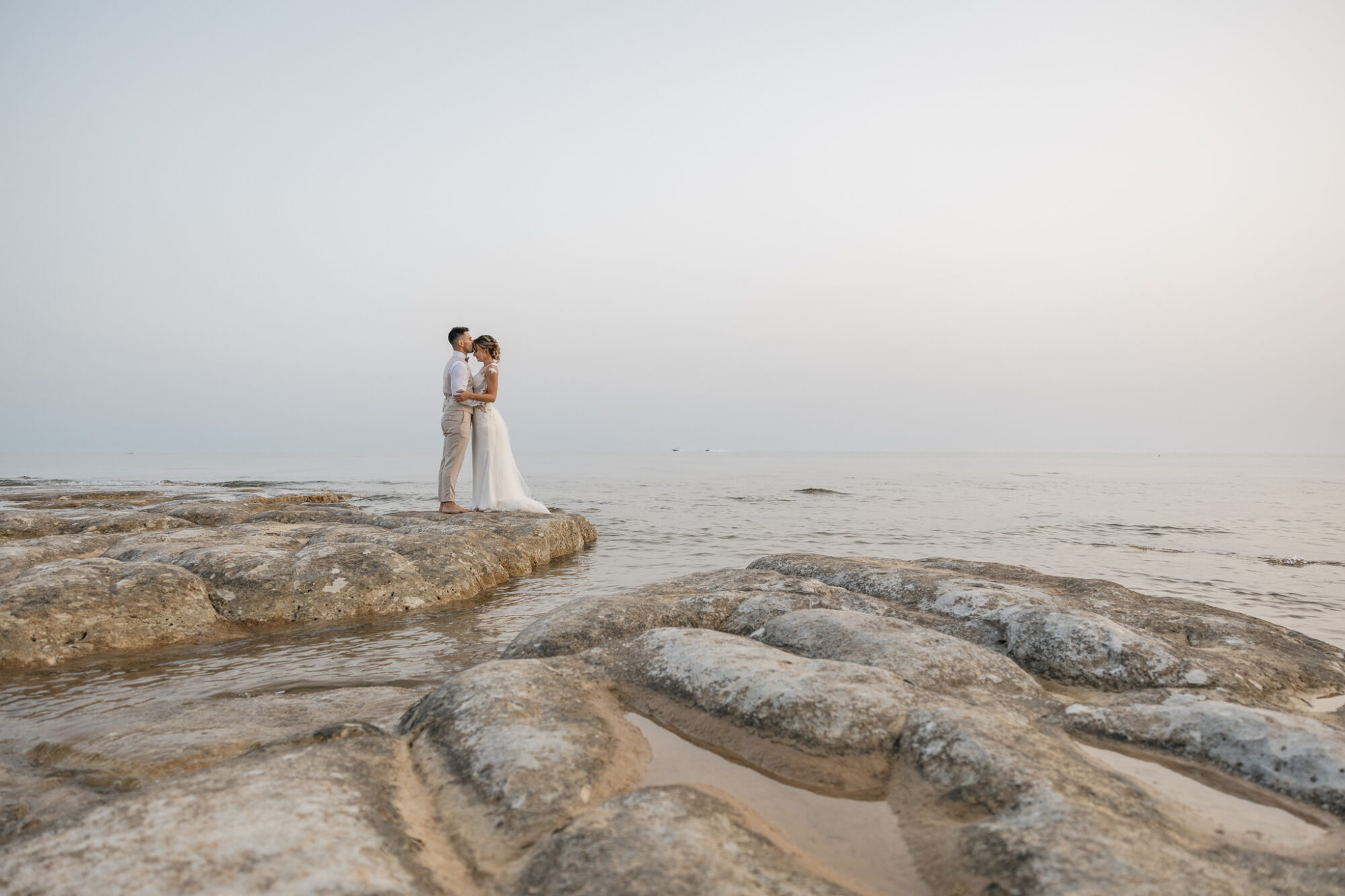 Ritratti di sposi che si guardano intensamente, in posa su scogli di marna bianca con il mare cristallino sullo sfondo. Fotografo matrimonio Daniele Pullara.