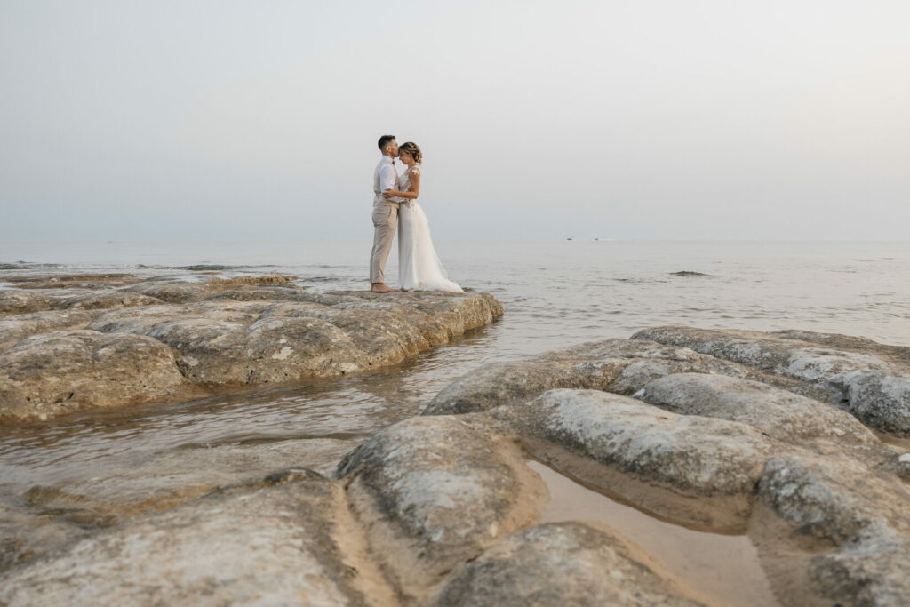 Ritratti di sposi che si guardano intensamente, in posa su scogli di marna bianca con il mare cristallino sullo sfondo. Fotografo matrimonio Daniele Pullara.
