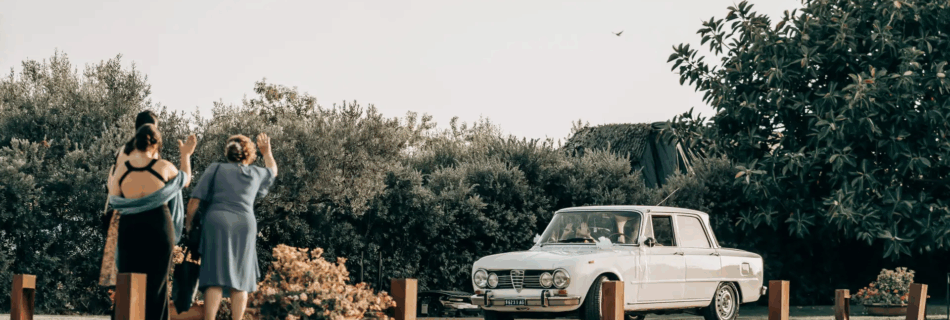 Vintage car wedding reportage with three guests waving in Sicily. Destination Wedding Photographer Daniele Pullara.