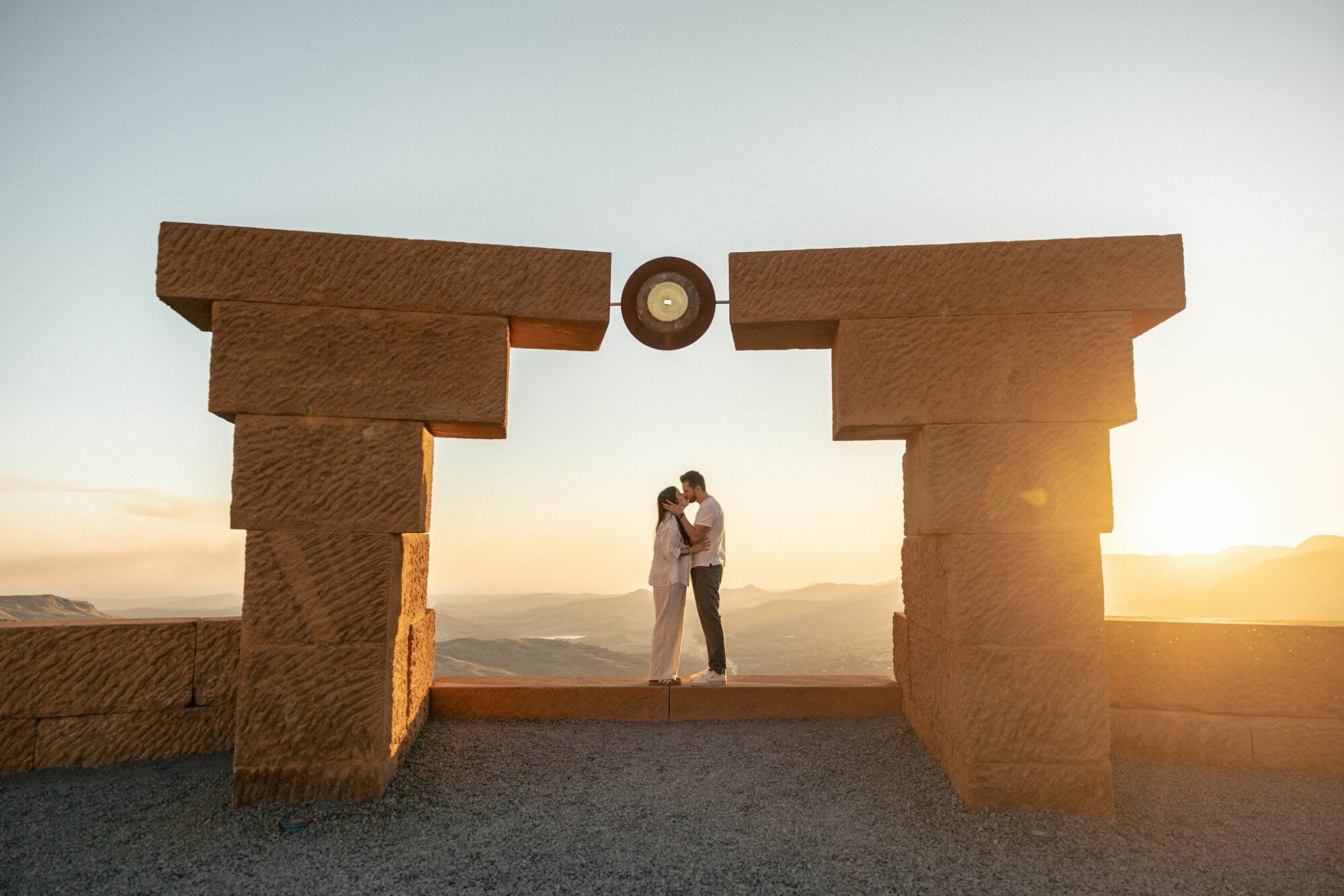 Couple kissing at sunset at Teatro di Andromeda in Sicily during a surprise marriage proposal, overlooking the hills.