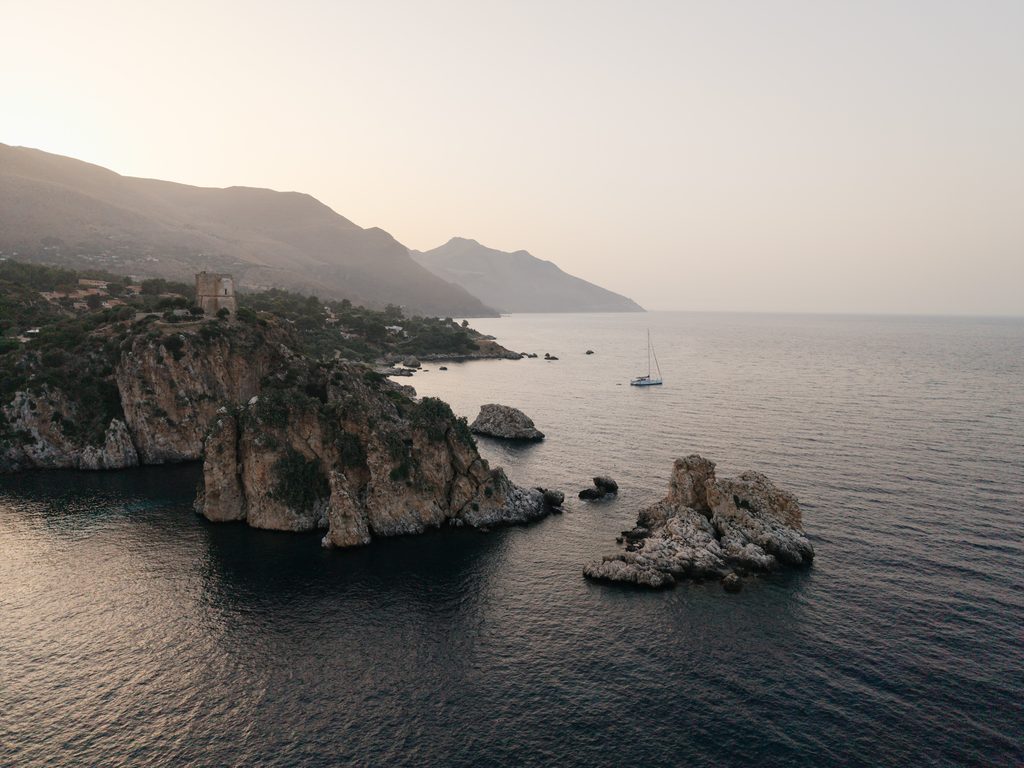 Scopello coastline and sea stacks in the evening with a sailing boat on the Mediterranean