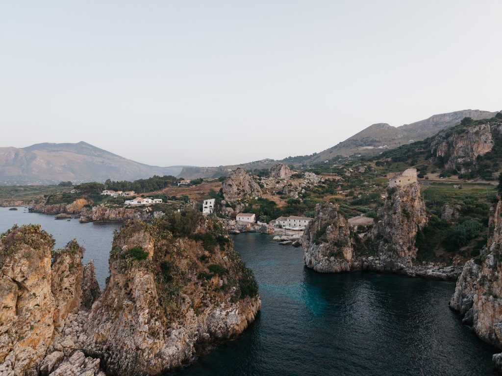 Aerial view of Scopello bay with sea stacks, rocky cliffs and Tonnara di Scopello in the background