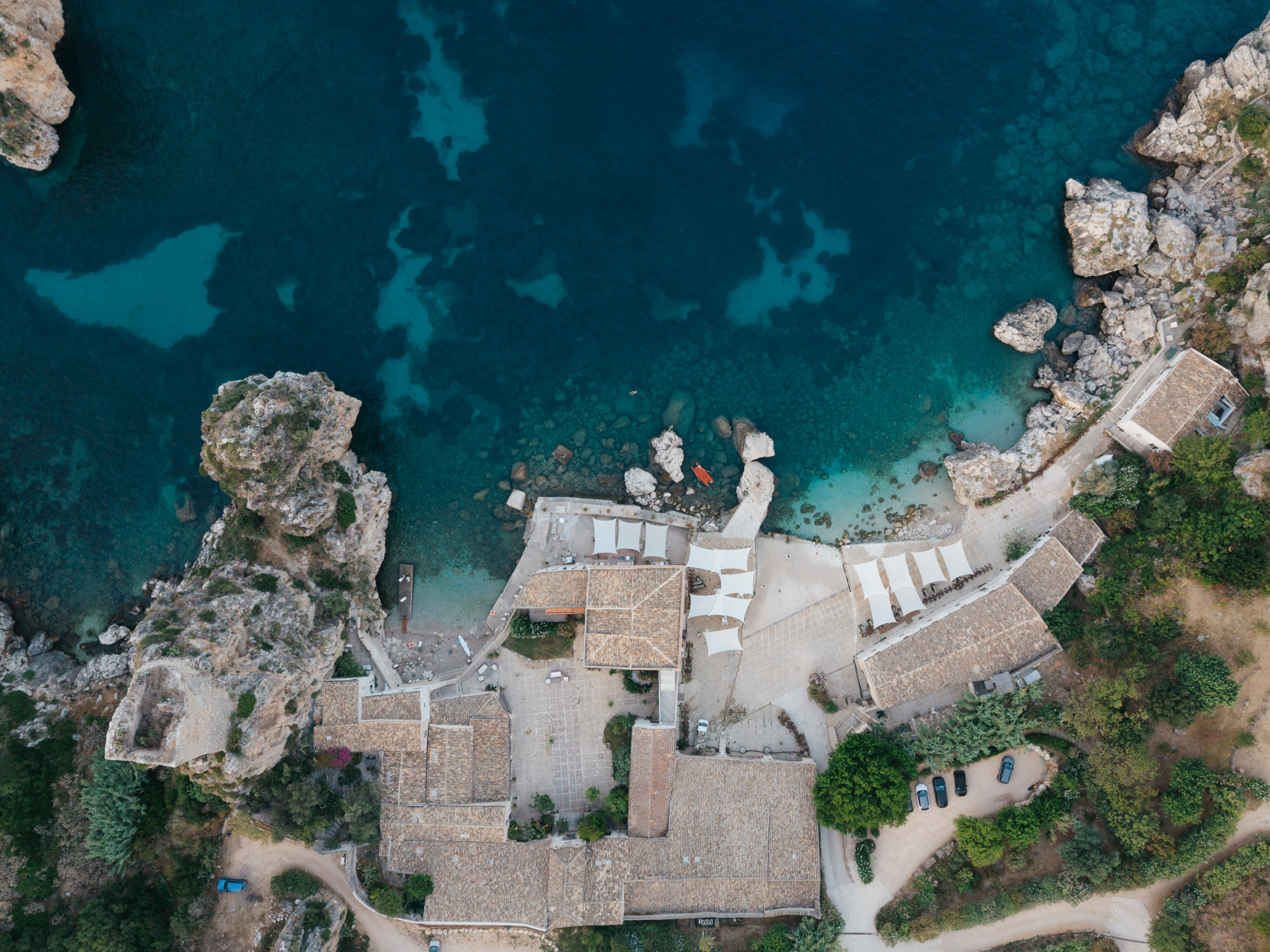 Top down aerial view of Tonnara di Scopello showing the buildings, courtyards, rocky coast and sea